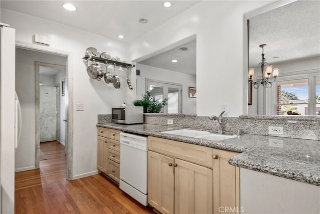 kitchen with light stone countertops, white dishwasher, wood-type flooring, sink, and a notable chandelier