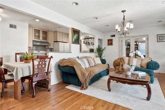 living room with an inviting chandelier, light wood-type flooring, and a textured ceiling