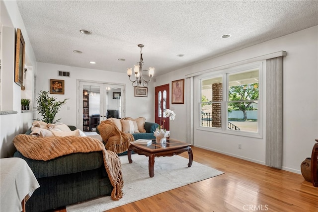 living room featuring light wood-type flooring, a chandelier, and a textured ceiling