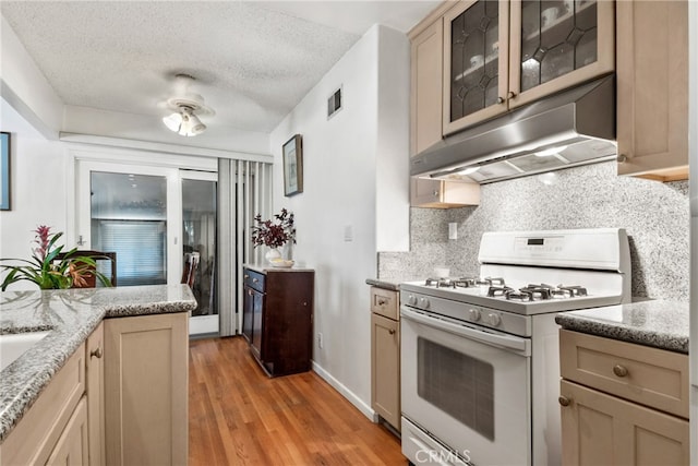 kitchen featuring white range with gas stovetop, backsplash, a textured ceiling, light brown cabinetry, and light hardwood / wood-style flooring