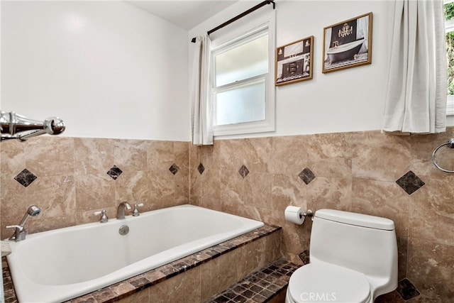 bathroom with a wealth of natural light, tiled bath, tile walls, and toilet