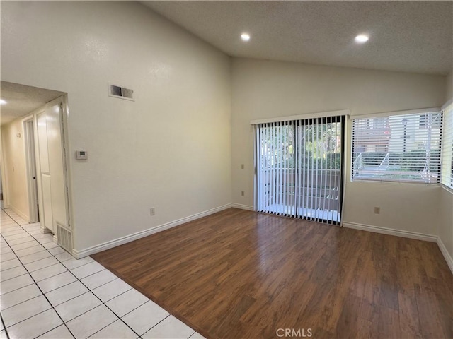 spare room featuring high vaulted ceiling, light hardwood / wood-style floors, and a textured ceiling