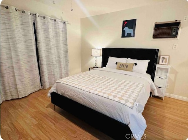 bedroom featuring baseboards, wood finished floors, and an AC wall unit