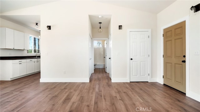 kitchen featuring white cabinets, lofted ceiling, light hardwood / wood-style floors, and decorative light fixtures