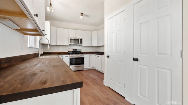 kitchen featuring sink, white cabinetry, stainless steel appliances, light hardwood / wood-style floors, and wood counters