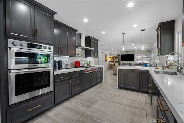 kitchen featuring wall chimney range hood, stainless steel appliances, backsplash, sink, and light stone counters