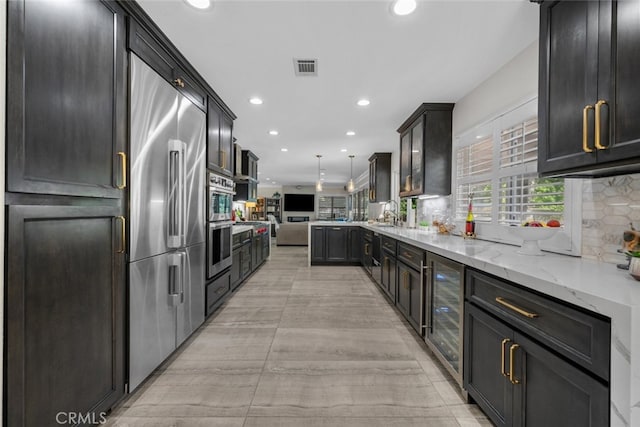 kitchen featuring stainless steel built in refrigerator, beverage cooler, backsplash, light stone countertops, and pendant lighting