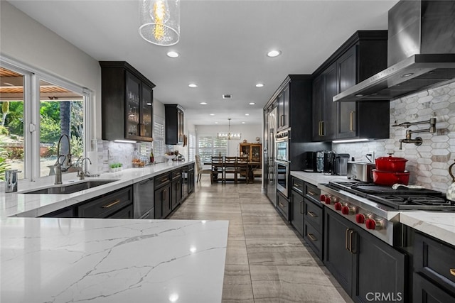 kitchen featuring a healthy amount of sunlight, wall chimney range hood, sink, and pendant lighting