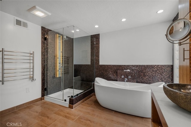 bathroom featuring a textured ceiling, separate shower and tub, radiator, tile walls, and vanity