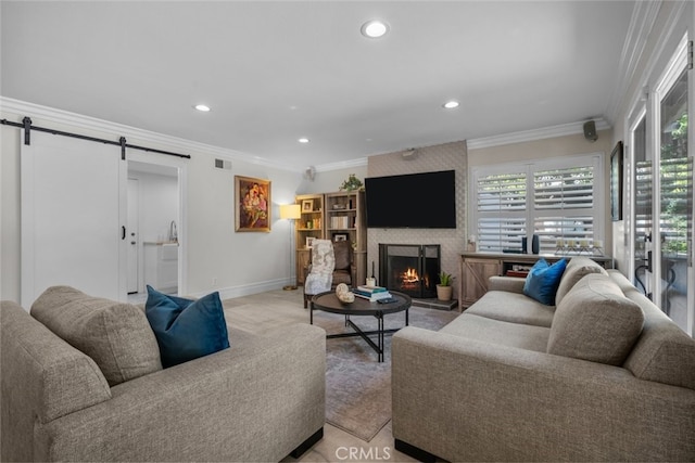 living room with ornamental molding, a barn door, and a large fireplace