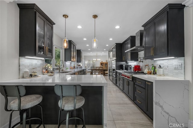 kitchen featuring wall chimney range hood, kitchen peninsula, backsplash, sink, and pendant lighting