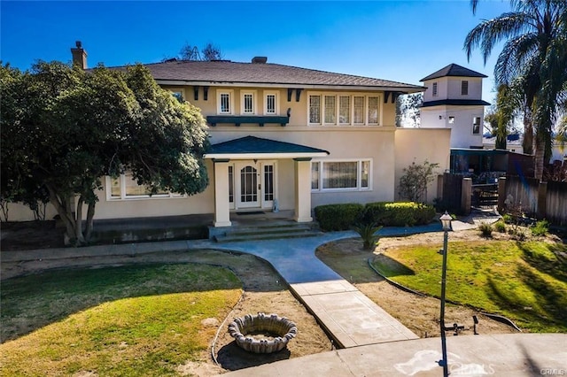 view of front of house featuring french doors, stucco siding, fence, and a front lawn