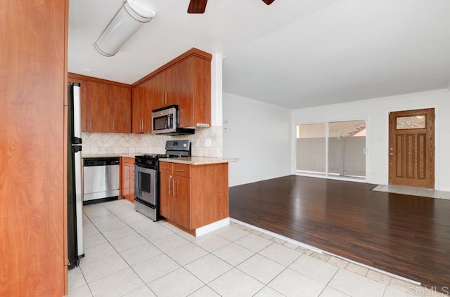 kitchen featuring crown molding, decorative backsplash, ceiling fan, light wood-type flooring, and stainless steel appliances