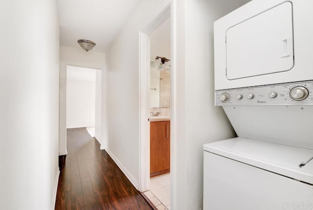 clothes washing area featuring sink, stacked washing maching and dryer, and dark wood-type flooring