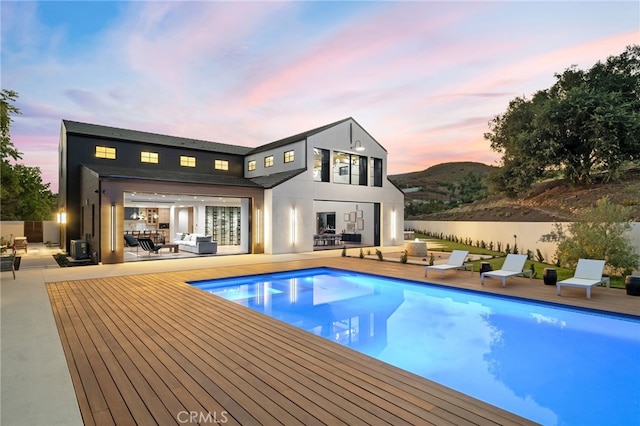 back house at dusk featuring a patio area and a swimming pool side deck with water view