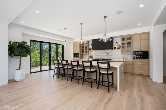 kitchen with a large island, light brown cabinetry, hanging light fixtures, and light hardwood / wood-style floors