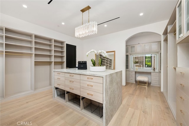 spacious closet with built in desk, light hardwood / wood-style floors, and an inviting chandelier