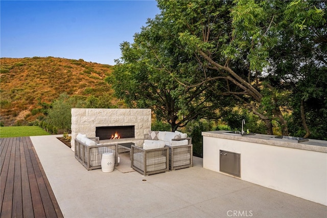 view of patio / terrace featuring an outdoor living space with a fireplace, sink, and a deck with mountain view