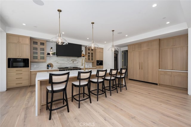 kitchen with pendant lighting, light hardwood / wood-style floors, backsplash, and a large island with sink