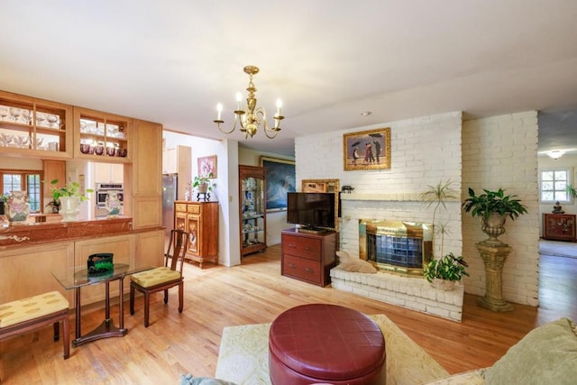 living room featuring a brick fireplace, light hardwood / wood-style floors, and a notable chandelier