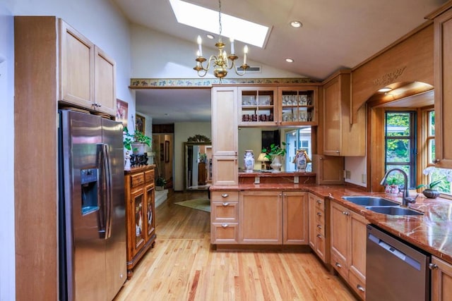 kitchen featuring sink, hanging light fixtures, stainless steel appliances, light hardwood / wood-style flooring, and vaulted ceiling with skylight