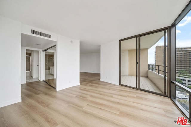 unfurnished room with light hardwood / wood-style flooring, a wall of windows, and plenty of natural light