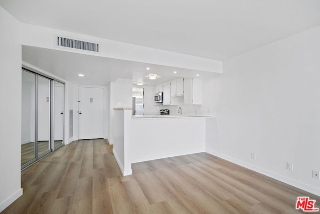 interior space with sink, light hardwood / wood-style flooring, kitchen peninsula, and white cabinetry