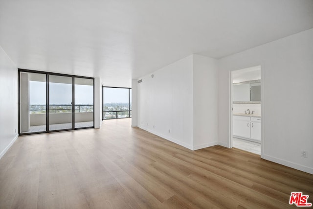 empty room with light wood-type flooring, sink, and floor to ceiling windows