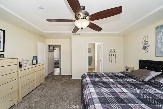 bedroom with a tray ceiling, dark carpet, connected bathroom, and ceiling fan