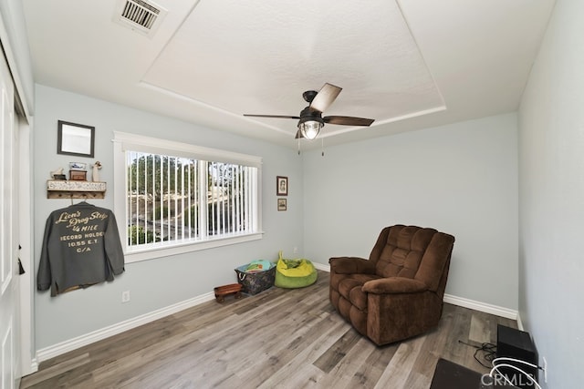 sitting room featuring a raised ceiling, ceiling fan, and wood-type flooring