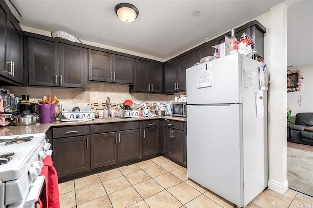 kitchen featuring white appliances, light tile patterned flooring, sink, dark brown cabinetry, and decorative backsplash