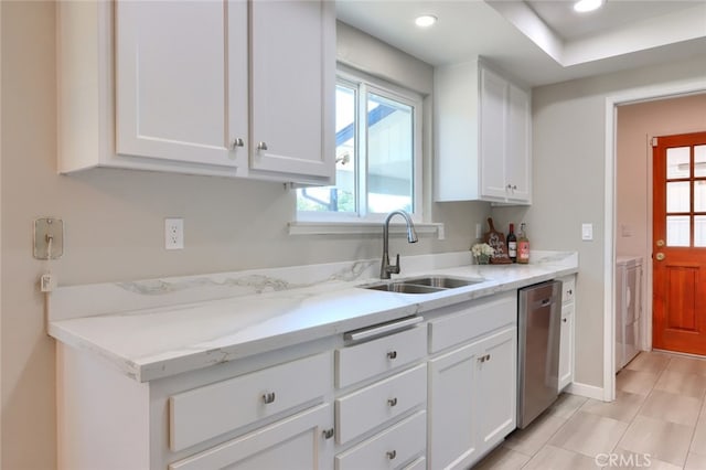 kitchen with light stone counters, white cabinets, washer / dryer, stainless steel dishwasher, and sink