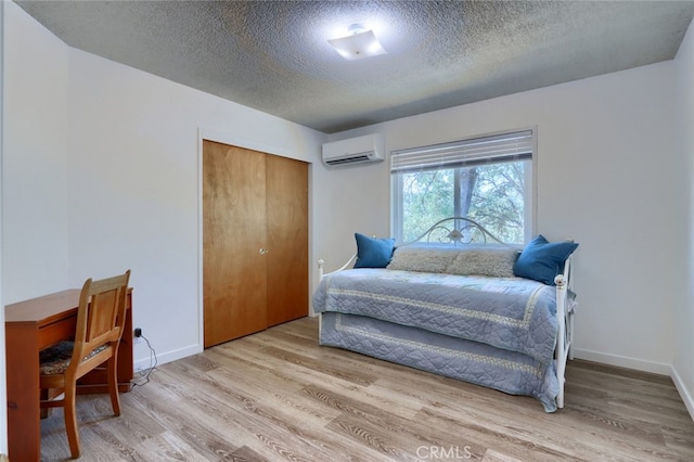 bedroom featuring an AC wall unit, light wood-type flooring, a closet, and a textured ceiling