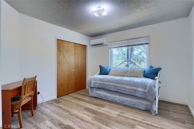 bedroom with a wall unit AC, baseboards, a textured ceiling, a closet, and wood finished floors