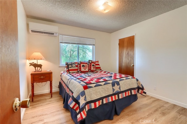 bedroom with baseboards, a wall unit AC, light wood-style floors, and a textured ceiling