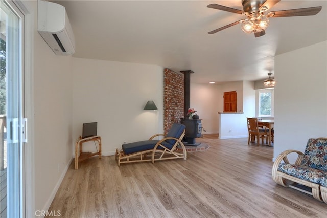 sitting room featuring a wall mounted air conditioner, light wood finished floors, baseboards, ceiling fan, and a wood stove