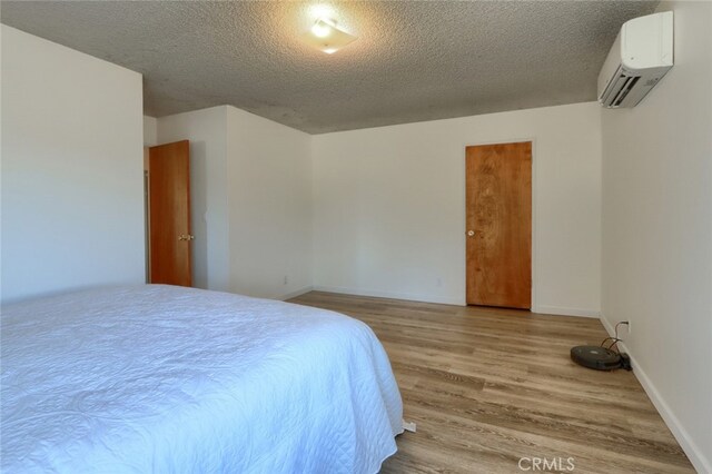 bedroom featuring light wood-type flooring, a textured ceiling, and an AC wall unit