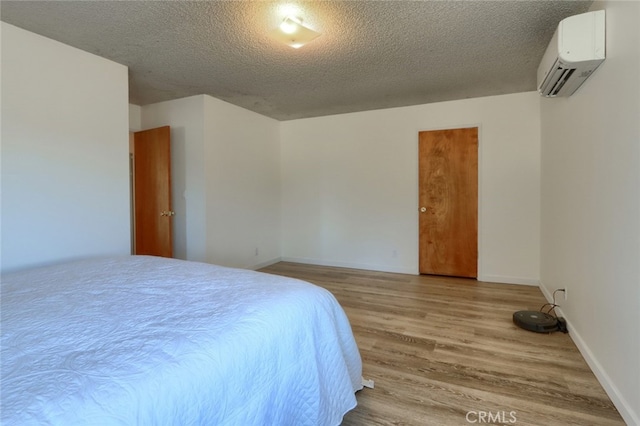 bedroom featuring baseboards, wood finished floors, an AC wall unit, and a textured ceiling