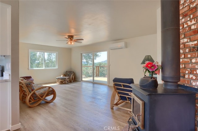 living area with a wall unit AC, wood finished floors, a wood stove, and a ceiling fan