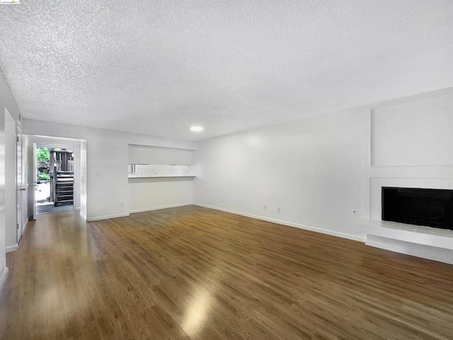 unfurnished living room with a textured ceiling, a large fireplace, and dark wood-type flooring