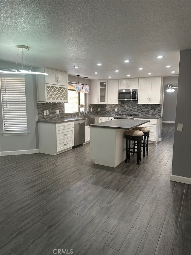 kitchen with pendant lighting, white cabinetry, appliances with stainless steel finishes, a center island, and dark hardwood / wood-style flooring