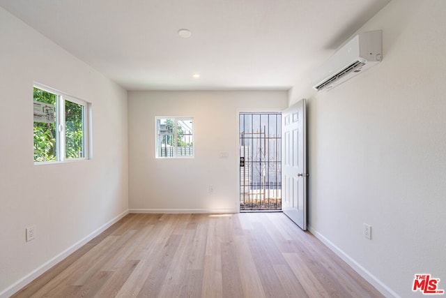 spare room with light hardwood / wood-style floors, a wall unit AC, and a wealth of natural light