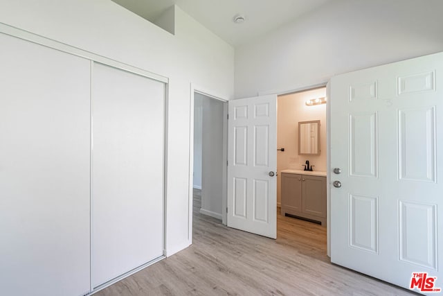 unfurnished bedroom featuring a high ceiling, light wood-type flooring, a closet, sink, and connected bathroom