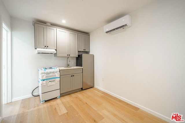 kitchen featuring light wood-type flooring, sink, a wall mounted AC, gray cabinets, and white range