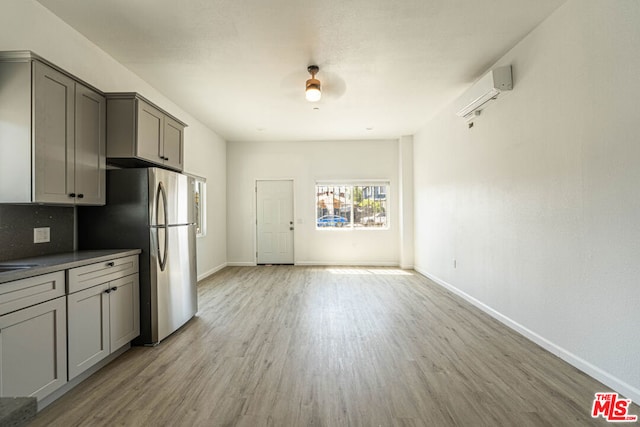 kitchen featuring a wall unit AC, stainless steel fridge, gray cabinetry, light hardwood / wood-style flooring, and decorative backsplash