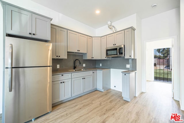 kitchen with tasteful backsplash, sink, light hardwood / wood-style floors, appliances with stainless steel finishes, and gray cabinets