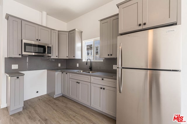 kitchen featuring light wood-type flooring, stainless steel appliances, tasteful backsplash, sink, and gray cabinets