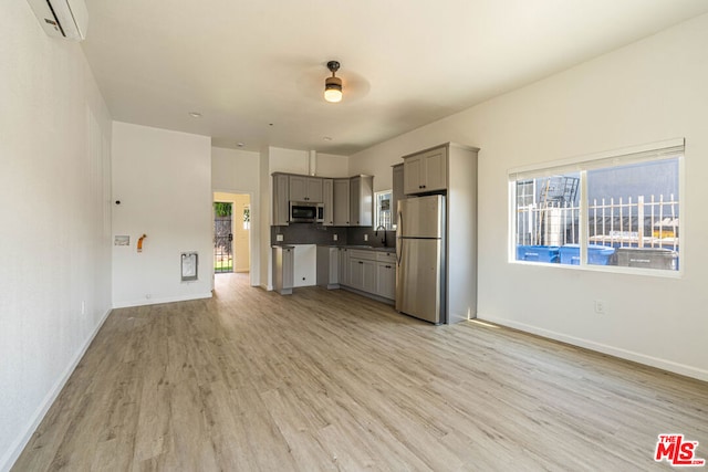 kitchen with gray cabinets, light wood-type flooring, stainless steel appliances, backsplash, and a wall mounted air conditioner