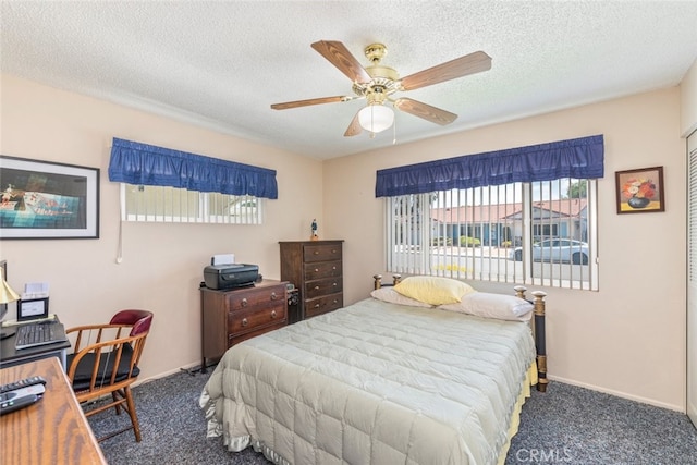 bedroom with a textured ceiling, dark carpet, and ceiling fan