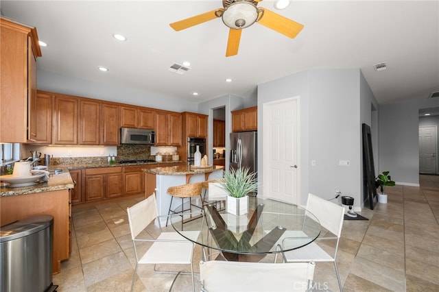 kitchen featuring a center island, appliances with stainless steel finishes, decorative backsplash, a kitchen breakfast bar, and light stone counters